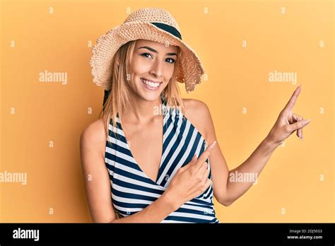 Belle femme blonde portant un chapeau d été souriant et regardant la caméra pointant avec deux