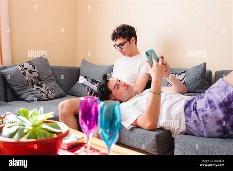 Snuggling Latin Gay Couple In Pajama Sharing Their Hobbies On Sofa On