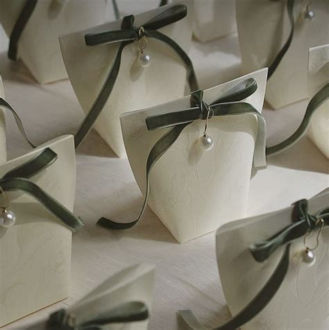 Many Small White Boxes With Green Ribbons Tied Around The Edges And Pearls On Them Sitting On A