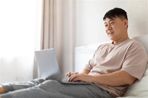 Happy Mature Asian Man Using Laptop In Bed Copy Space Stock Photo