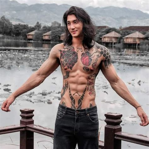 A Man With Long Hair And Tattoos On His Chest Standing In Front Of A