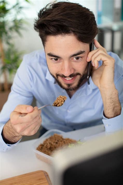 Businessman Having Lunch At Desk And Talking On Telephone Stock Photo