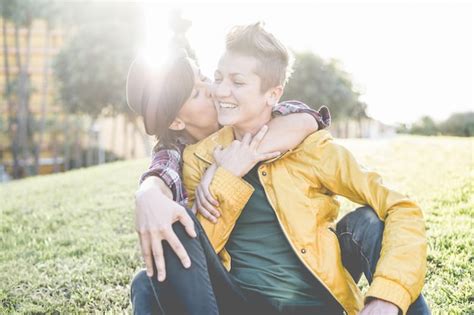 Feliz pareja gay que tiene momentos tiernos al aire libre sentado en el césped mujeres jóvenes