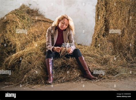 Blonde Woman In A Jacket And Boots Is Sitting On The Hay Stock Photo Alamy