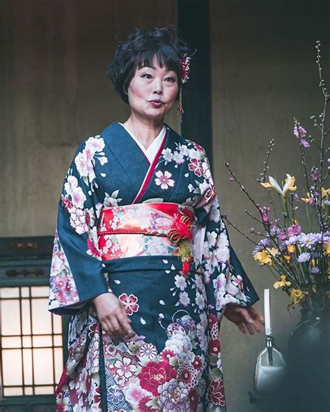 A Woman In A Kimono Standing Next To A Vase With Flowers