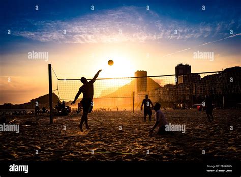 Silhouettes Of Men Playing Beach Volleyball By Sunset In Copacabana