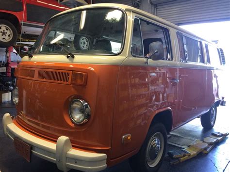 An Orange Van Parked In A Garage Next To Other Vehicles And People