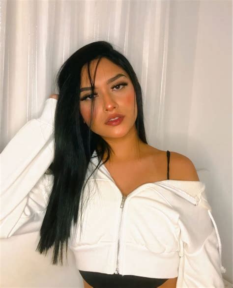 A Woman With Long Black Hair Wearing A White Top And Black Panties Posing For The Camera