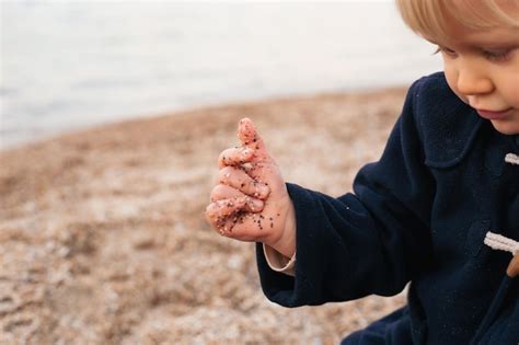 Niño jugando con arena en la playa cerca del mar en otoño o verano