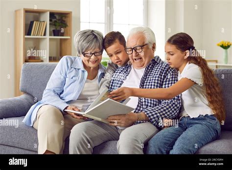 Grandparents Reading A Book To Their Grandchildren Sitting At Sofa At