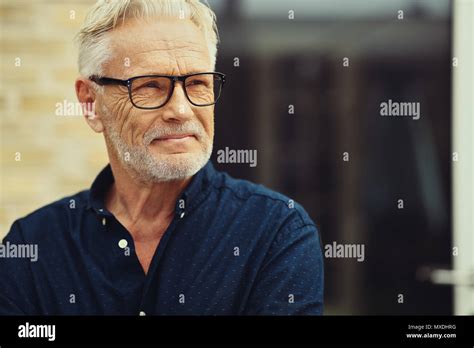 Senior Man With A Beard And Wearing Glasses Smiling Contently While