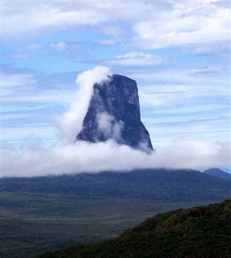 A Tall Mountain Towering Over A Lush Green Forest Filled With Lots Of