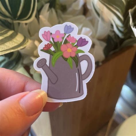 A Hand Holding A Sticker With Flowers In A Watering Can