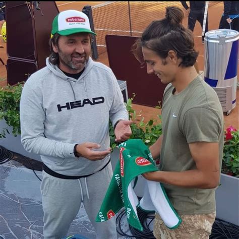 Two People Standing Next To Each Other Near A Tennis Court