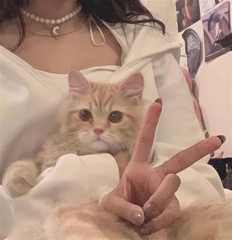 A Woman Is Holding A Cat In Her Lap And Making The V Sign With Her Fingers