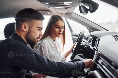 Woman testing car by help of male assistant indoors in the salon ...