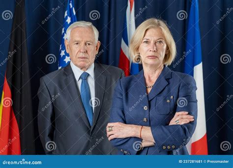 Two Mature Political Leaders In Formalwear Standing Against Four Flags