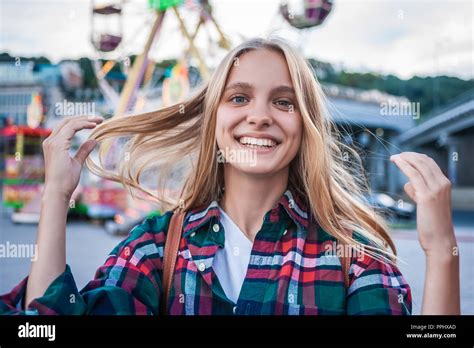 Happy Blonde Girl Smiling At Camera While Spending Time In Amusement Park Stock Photo Alamy