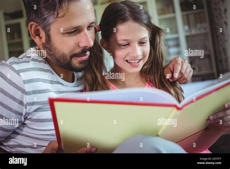 Smiling Father And Daughter Looking At Photo Album In Living Room Stock