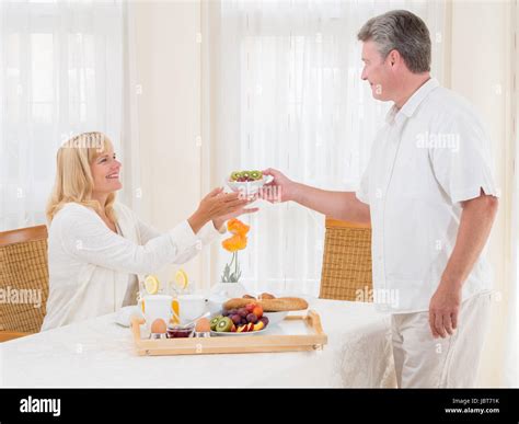 Mature Senior Husband Serving His Wife Healthy Breakfast Passing Her A Bowl Of Cereal Off The