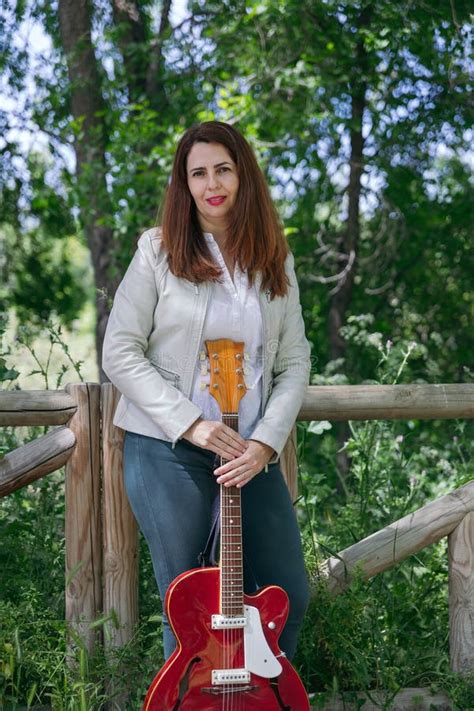 Mature Woman Posing With Her Red Acoustic Guitar In An Outdoor Park On