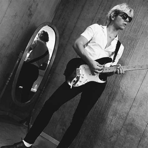 A Man With Sunglasses Playing An Electric Guitar In Front Of A Mirror