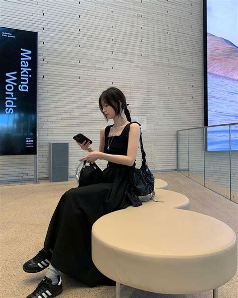 A Woman Sitting On Top Of A White Bench Next To A Wall Holding A Cell Phone