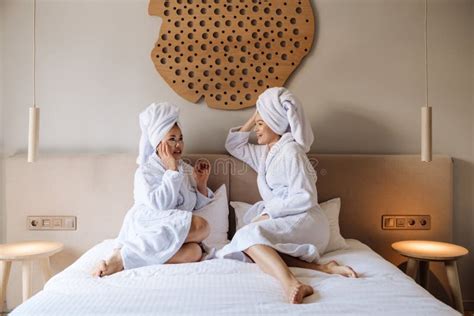 Two Attractive Women Wearing Bathrobes And Wrapped In Towels Using Eye Patches While Sitting On