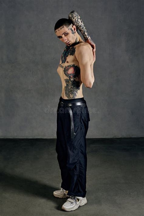 Strong Tattooed Fellow Naked Torso Beard Dressed In Black Pants White Sneakers Stretching