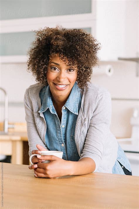 A Woman Leans On A Kitchen Counter Holding A Cup Of Coffee By