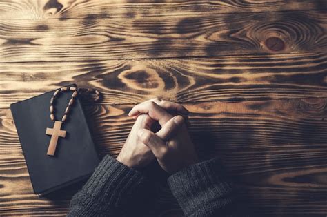 Cruz de la mano del hombre de oración en la santa biblia en la mesa de