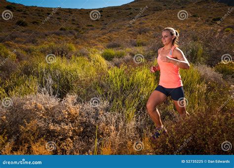 Blonde Female Trail Runner Running Through A Mountain Landscape Stock