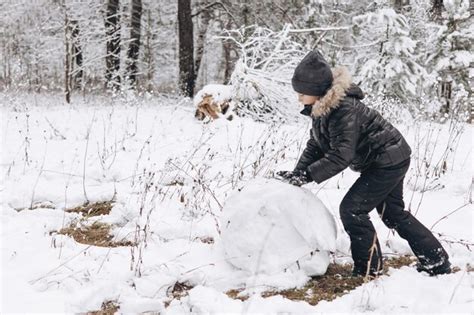 Criança feliz rolando grande bola de neve para boneco de neve na