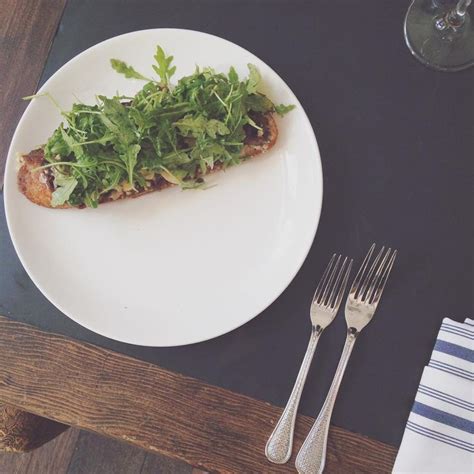 A White Plate Topped With Greens Next To A Fork And Knife On Top Of A Table