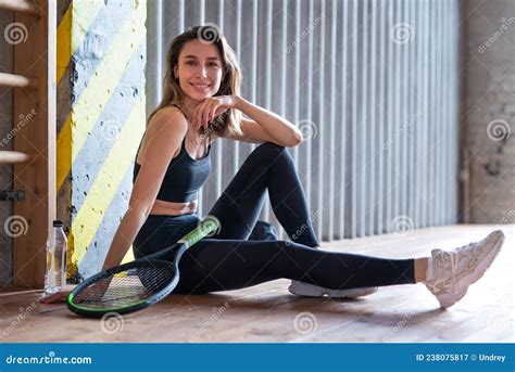 Portrait Of Female Tennis Player With Racket Sitting On Gym Floor Stock