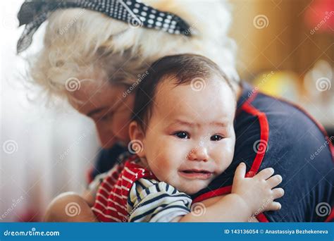 Grandmother Cradling Crying Infant Baby Girl Looking At Camera Stock