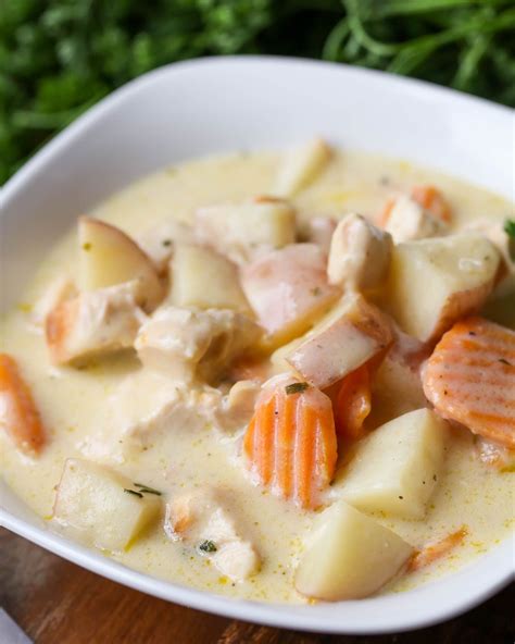 A White Bowl Filled With Chicken And Dumplings On Top Of A Wooden Table