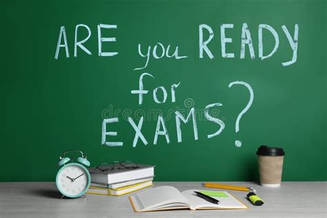 Different Stationery And Alarm Clock On Wooden Table Near Chalkboard