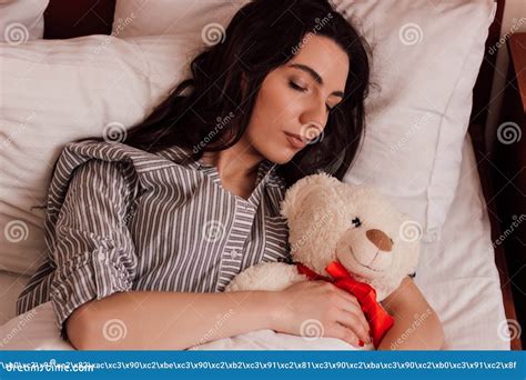 A Young Beautiful Girl Sleeps With A Teddy Bear In A Bed In Pajamas