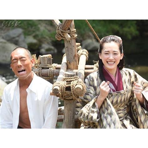 A Man And Woman Sitting Next To Each Other In Front Of A Wooden