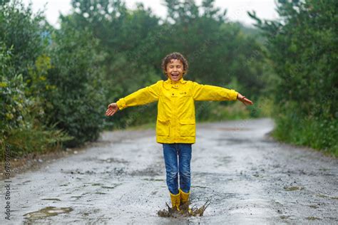 Kid playing in the rain in autumn park. Child jumping in muddy puddle ...