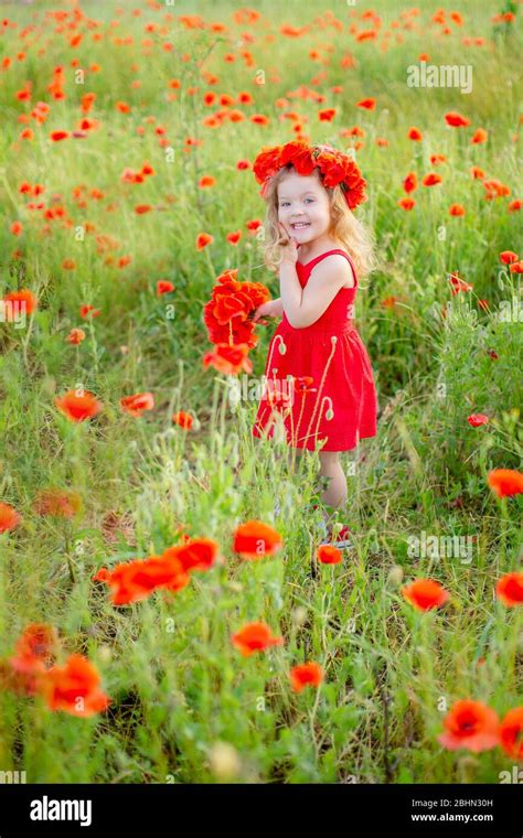 Kleine langhaarige blonde Mädchen in rotem Kleid auf dem Feld der Mohnblumen mit Kranz an ihrem