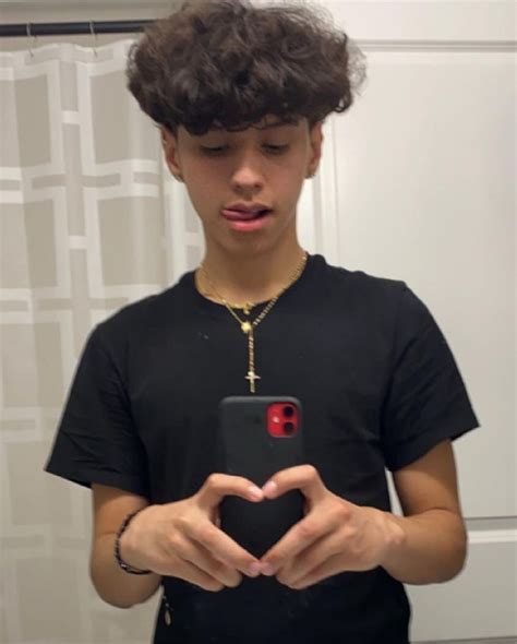 A Young Man Holding A Cell Phone In His Hands And Making A Heart Shape