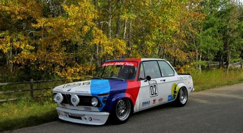 An Old Race Car Painted In Rainbow Colors On The Side Of The Road With