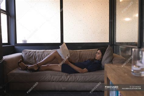 Businesswoman Lying On Sofa And Reading Document At Office Window