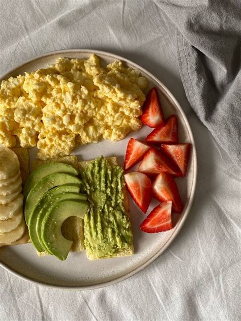 A White Plate Topped With Eggs Fruit And Avocado Next To Sliced