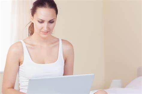 Premium Photo Smiling Brunette Sitting On Bed Using Her Laptop