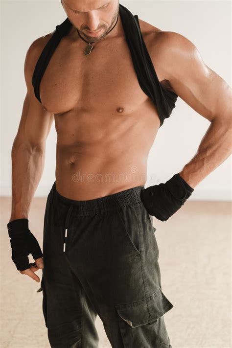 A Muscular Man With A Naked Torso In Orange Clothes Stands In A Room On A Light Background Stock