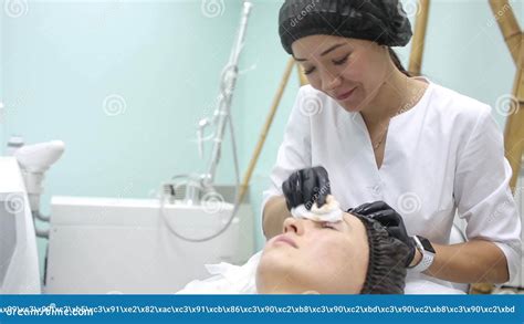 The Cosmetologist In Pink Gloves With A Brush Applies A Carbon Mask For