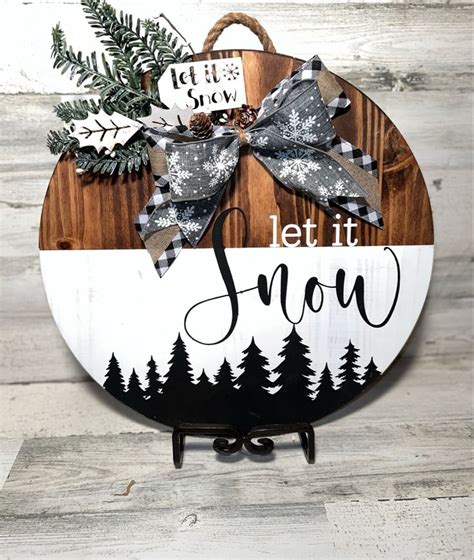 A Wooden Sign That Says Let It Snow With Pine Trees And Evergreens On